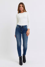 Load image into Gallery viewer, Model wearing a fitted long-sleeve white top and blue skinny jeans, paired with black heeled ankle boots, posed against a plain white background.